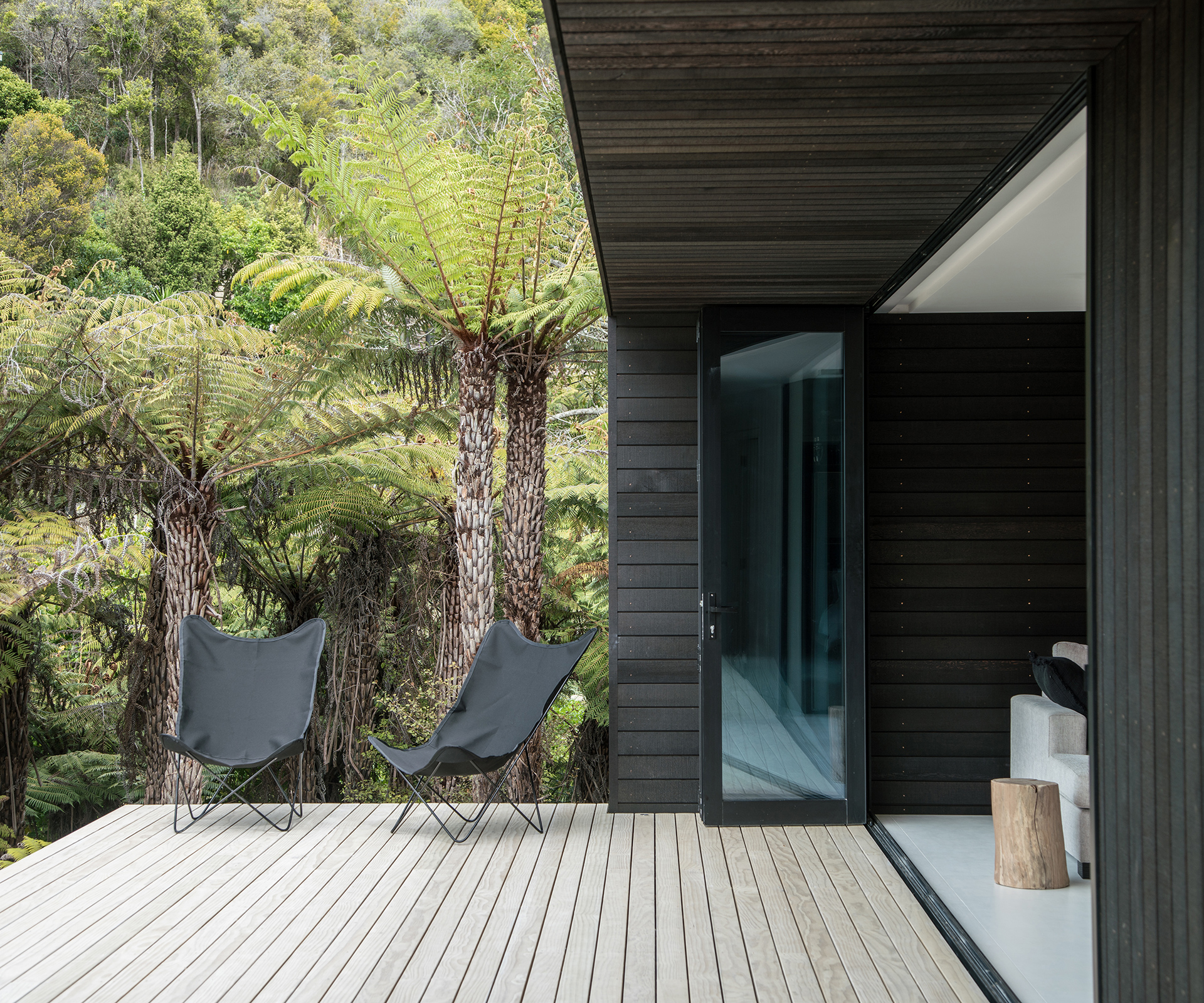 The home's dark cedar tones in with the punga ferns on the site. Bifold doors by Altherm Window Systems stack back to open the living areas to the view. Photograph by Jeremy Toth. 