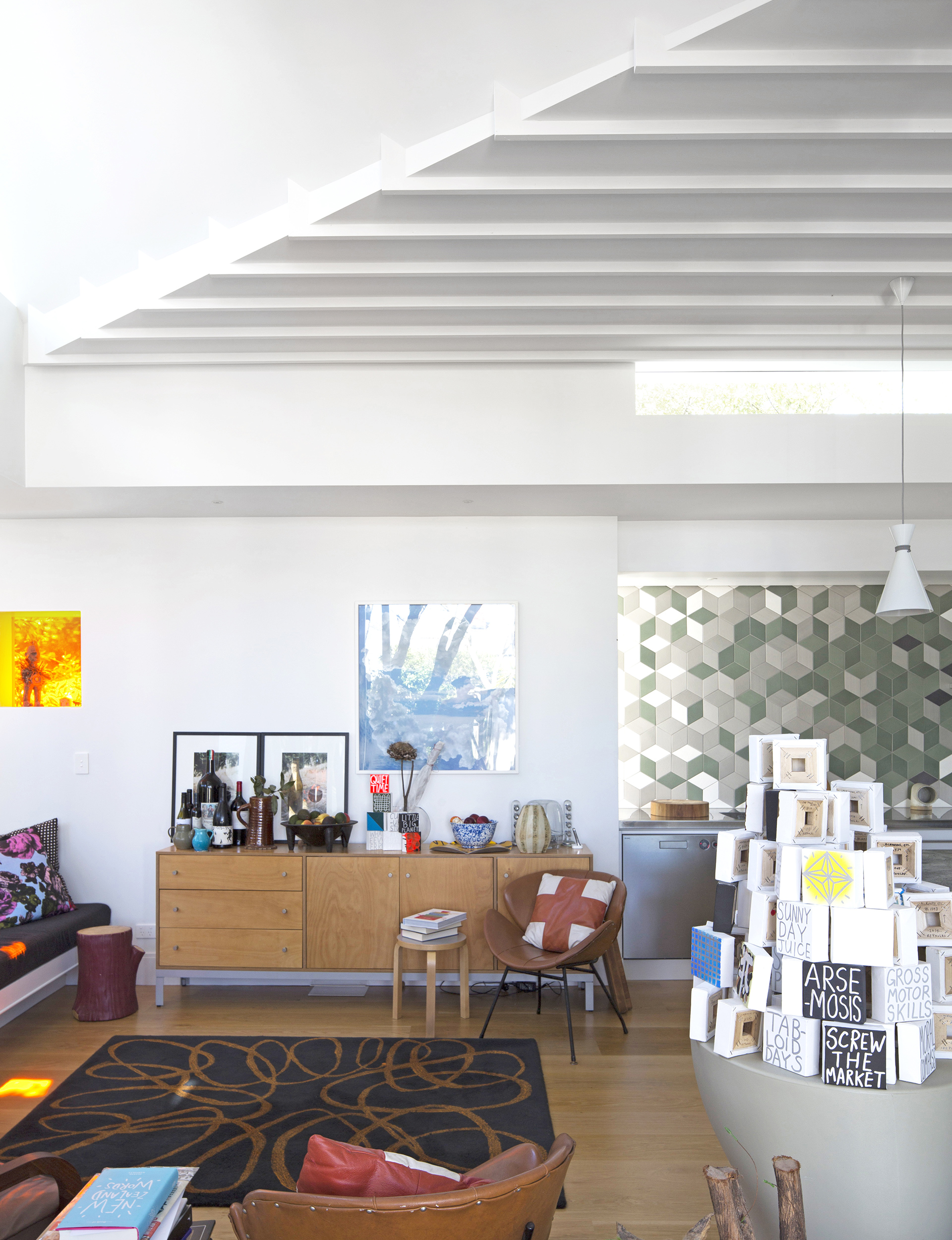 Bill Culbert photographs are propped up on the credenza by Michael Draper. The rug is from Dilana and features a drawing by John. The tan chairs are vintage. 