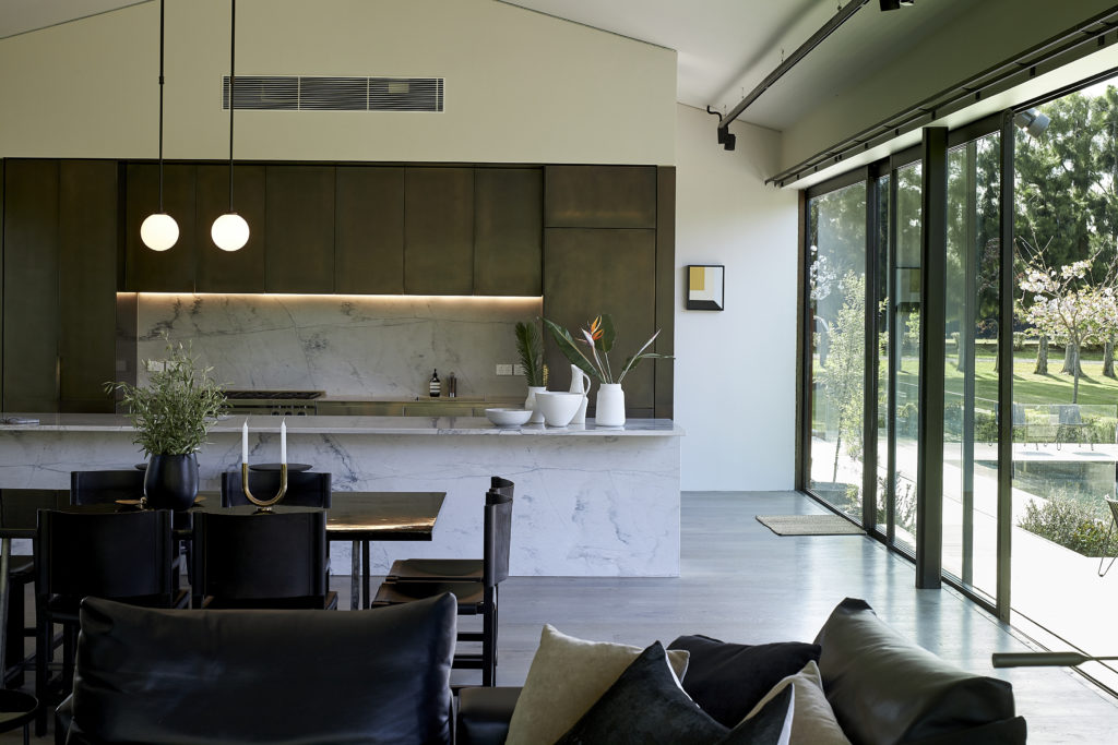 Open-plan kitchen, living, and dining areas are encased by large floor-to-ceiling glass panels and the valley outside.
