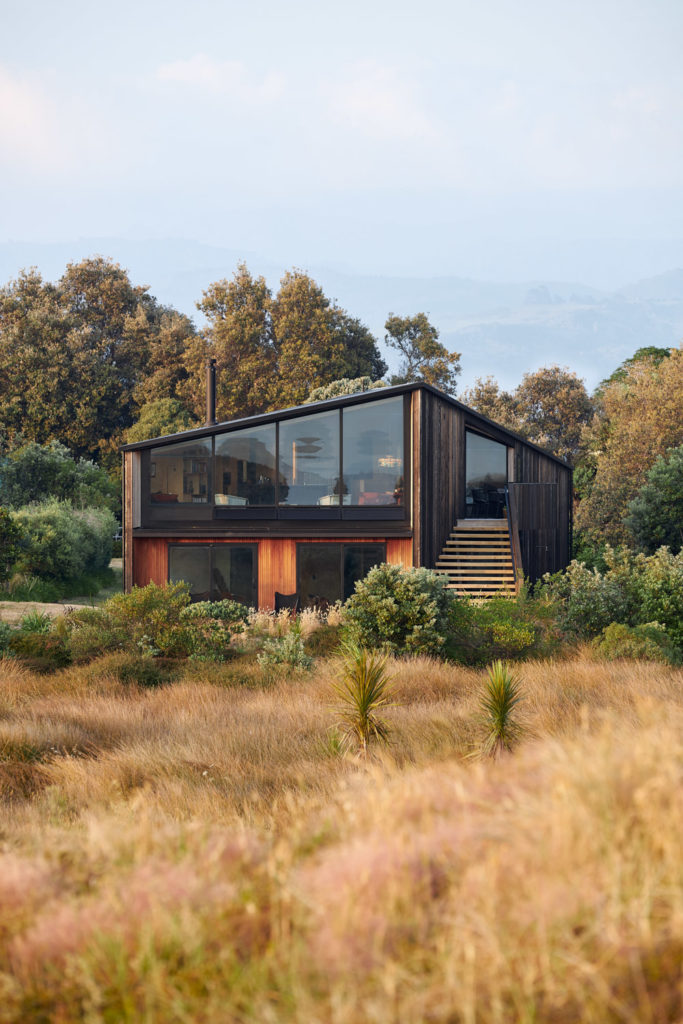 Outside view of the home, a contrast of dark and light wood. In the foreground: sand-coloured grass